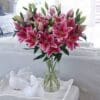 Here's an alt tag for the image: Pink lilies in a glass vase.