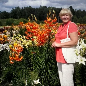 A woman standing beside vibrant orange and white flowers in a garden.