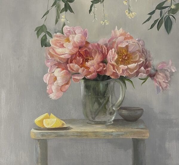 Soft pink flowers in a glass jug on a rustic table with lemon slices.